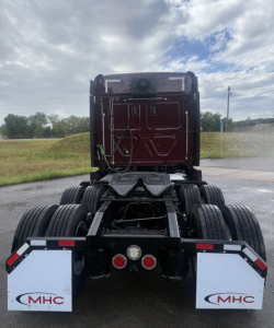 Truck rear view of a Freightliner Cascadia126 tractor chassis showing dual rear axles, mud flaps with MHC logo, and electrical lines near the cab base.