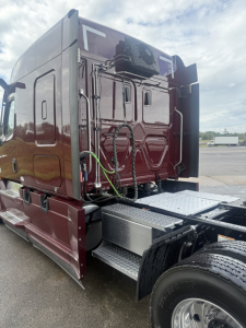 Freightliner Cascadia126 truck cab rear window area with exposed electrical wires and access panels; side steps and wheel visible.