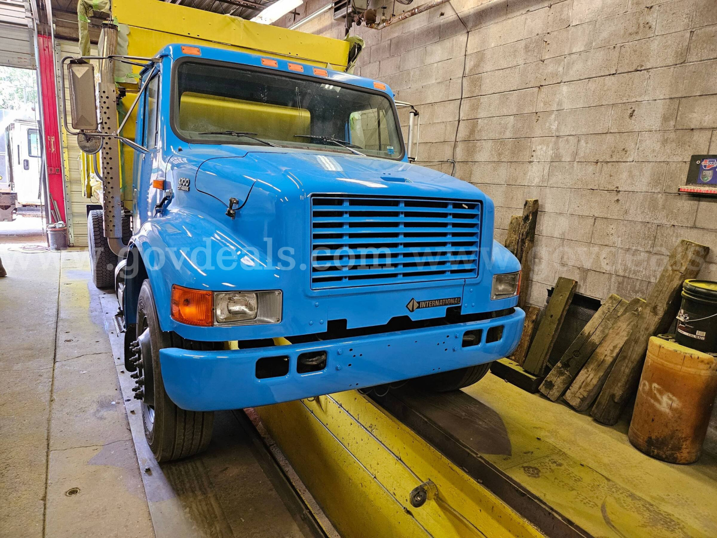 Blue 1999 International 4700 dump truck on a service lift with front view showing grille, headlights, and cab; VIN 1HTSCAAL4XH652469 and stock number 32136-37 visible in listing context.
