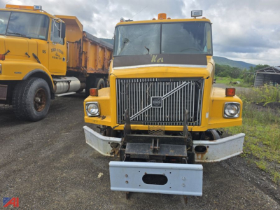 Volvo WG cab and chassis truck front view showing large grille, bumper, and salvage plate. Yellow paint with utility lights on roof.