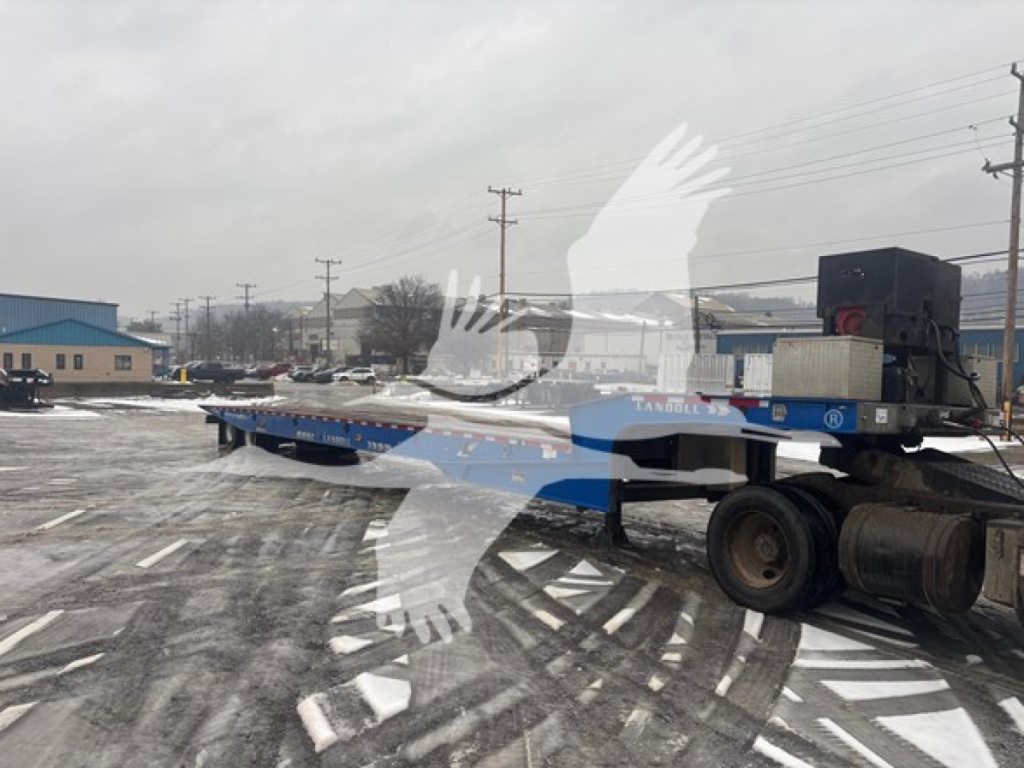 Trailer deck of a Landoll 440B traveling axle trailer attached to a semi truck in an industrial lot.