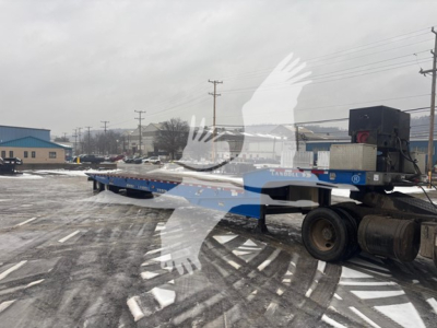 Trailer deck of a Landoll 440B traveling axle trailer attached to a semi truck in an industrial lot.