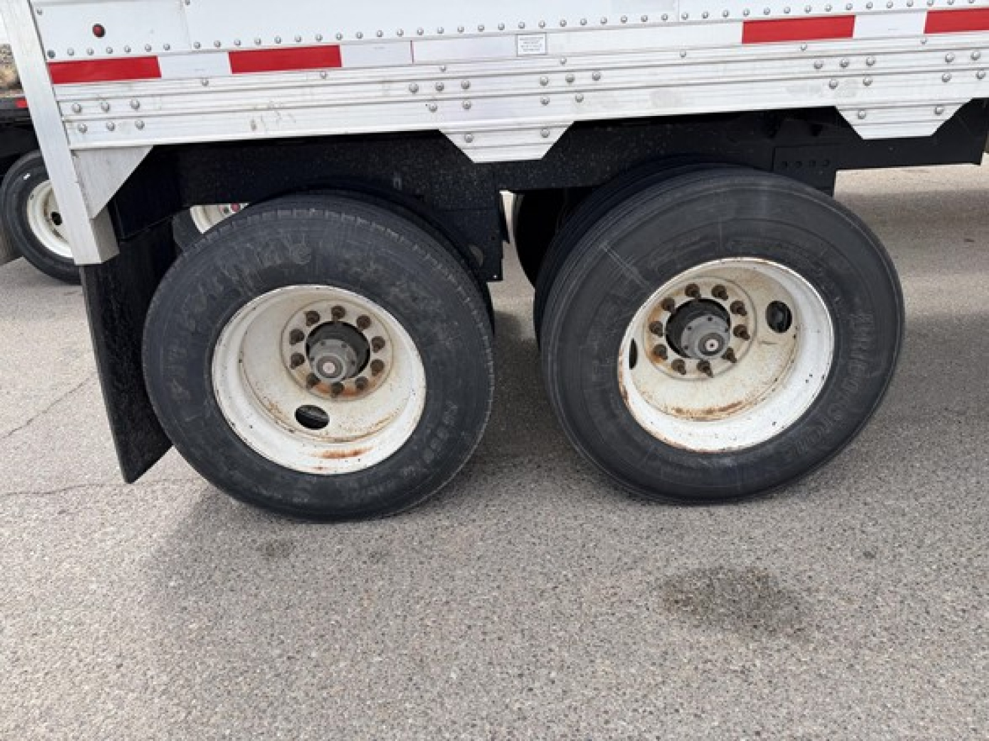 Timpte Super Hopper trailer wheels dual rear axles showing round white rims with black tires, side of trailer with riveted aluminum panels and red reflectors.