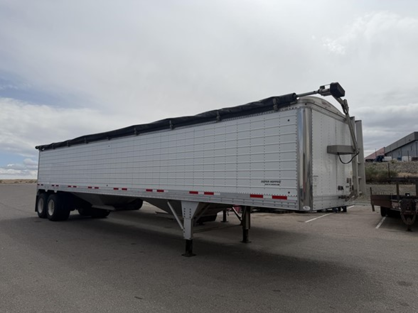 Trailer showing 2023 Timpte Super Hopper with silver aluminum body, dual rear axles, support legs down, and a tarp system rolled along top edge.