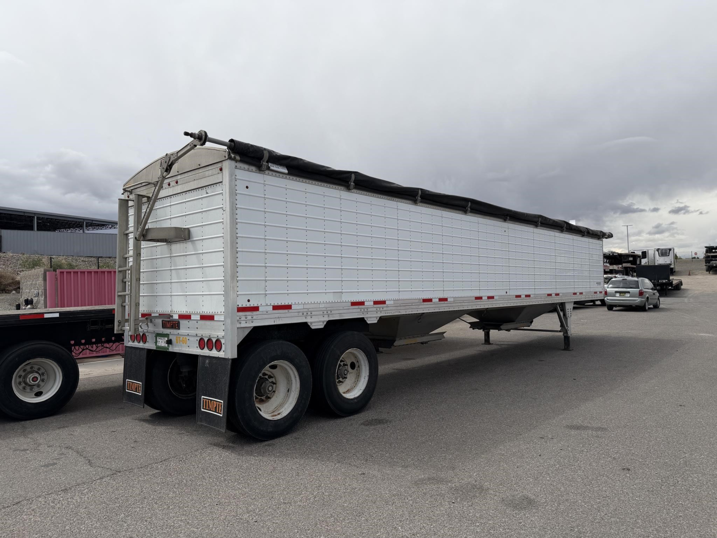 Timpte Super Hopper trailer showing long white aluminum side walls, covered top tarpaulin, triple-axle rear with tires, and rear lights.