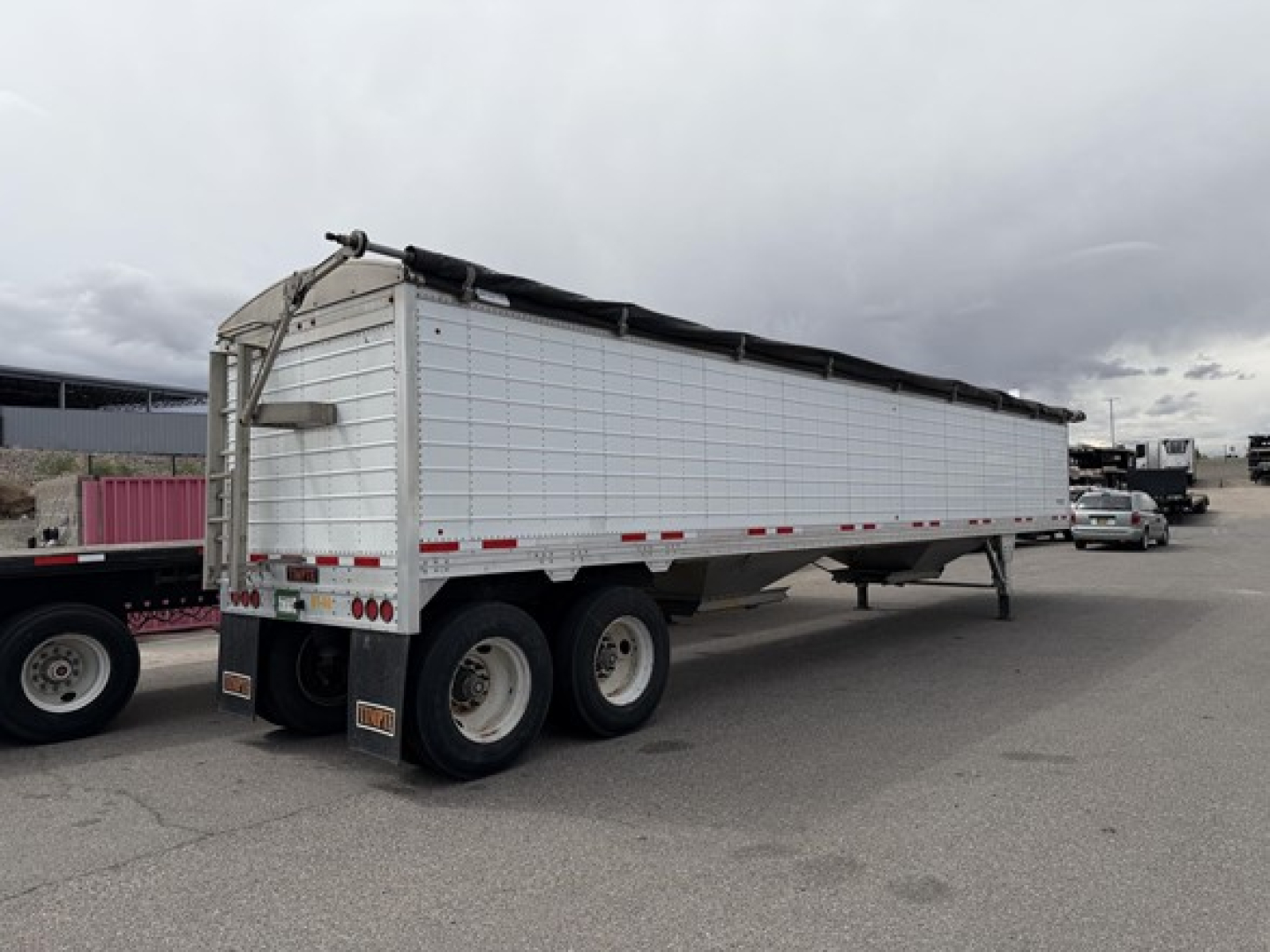 Trailer side view showing a white Timpte Super Hopper trailer with three axles and a black tarp cover.