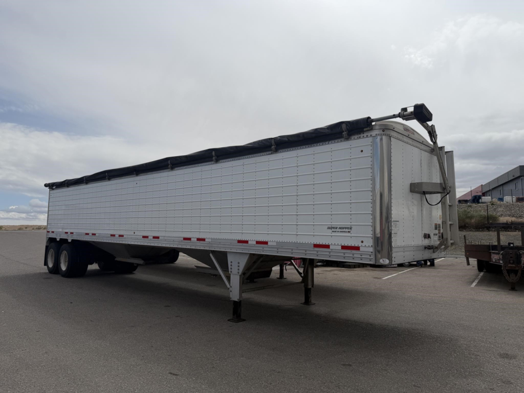 Trailer side view showing 2023 Timpte Super Hopper aluminum hopper with dual rear axles, long top tarp, and landing gear down.