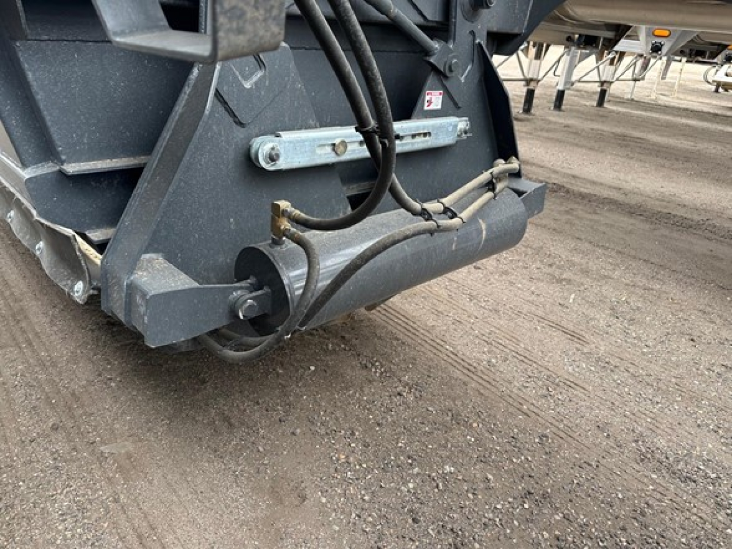Bottom-dump trailer hitch and rear undercarriage showing hydraulic hoses and frame hardware.