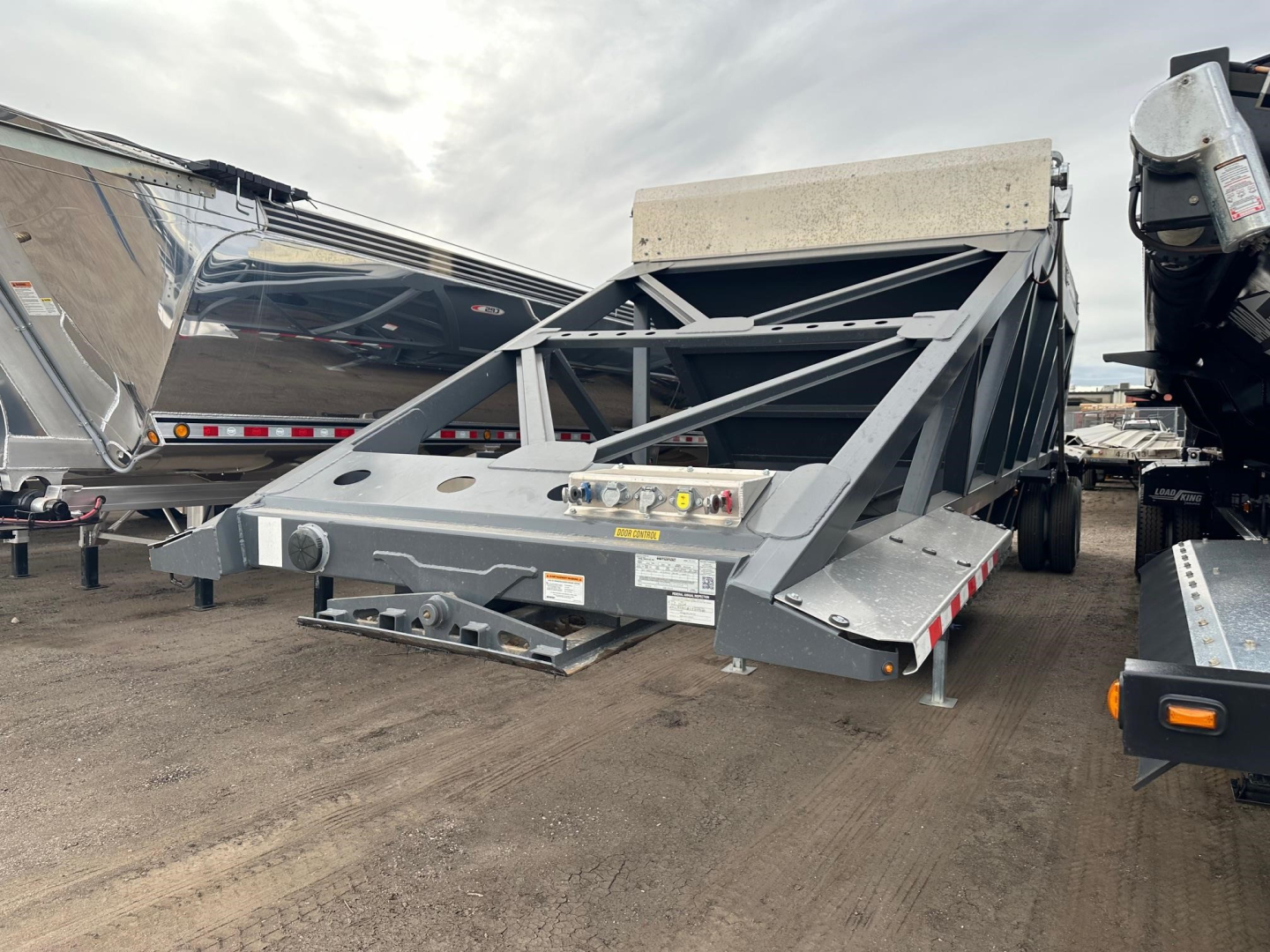 Bottom dump trailer frame showing steel structure with level indicators and platform, gray color, tilted hopper at rear, side ramps and hitching area visible.