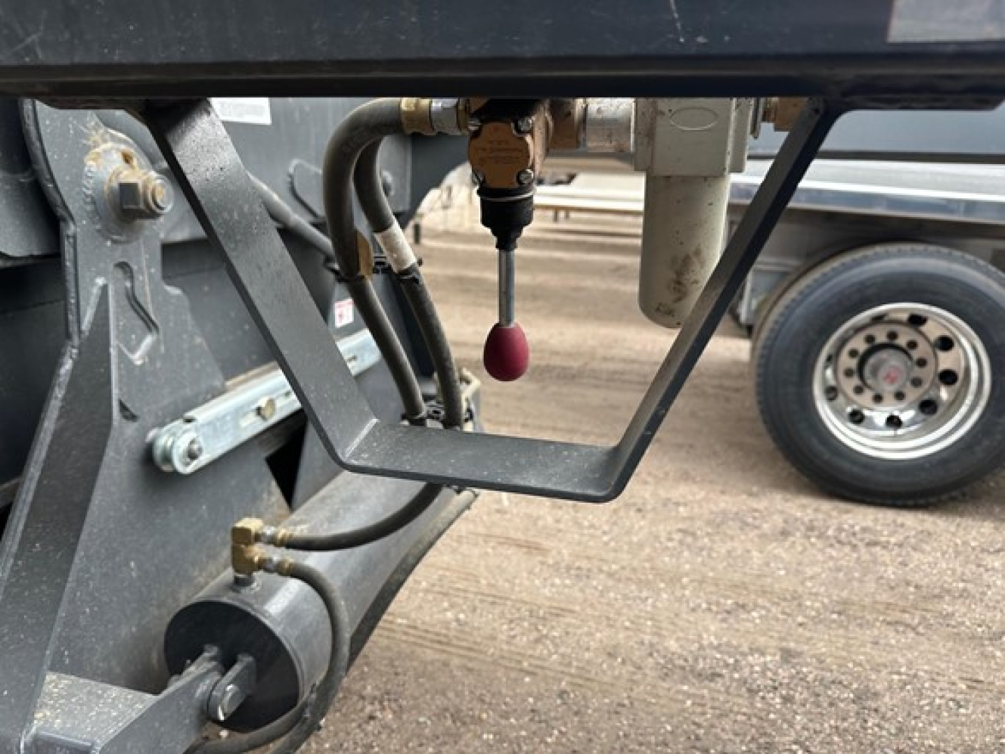 Trailer hydraulic lines and valve assembly under a 40' bottom dump trailer showing hydraulic hoses and a red pull pin.