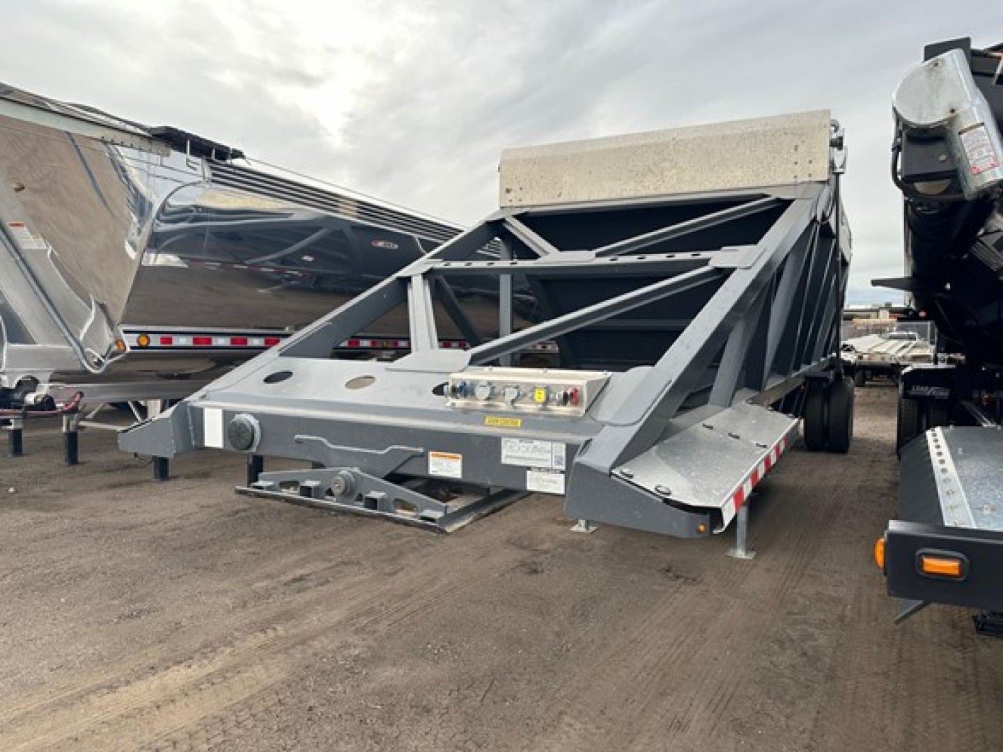 Truck trailer bottom dump with air ride system, gray metal frame, rear linkage, and control boxes. Visible text includes warning labels and small stickers on the frame.