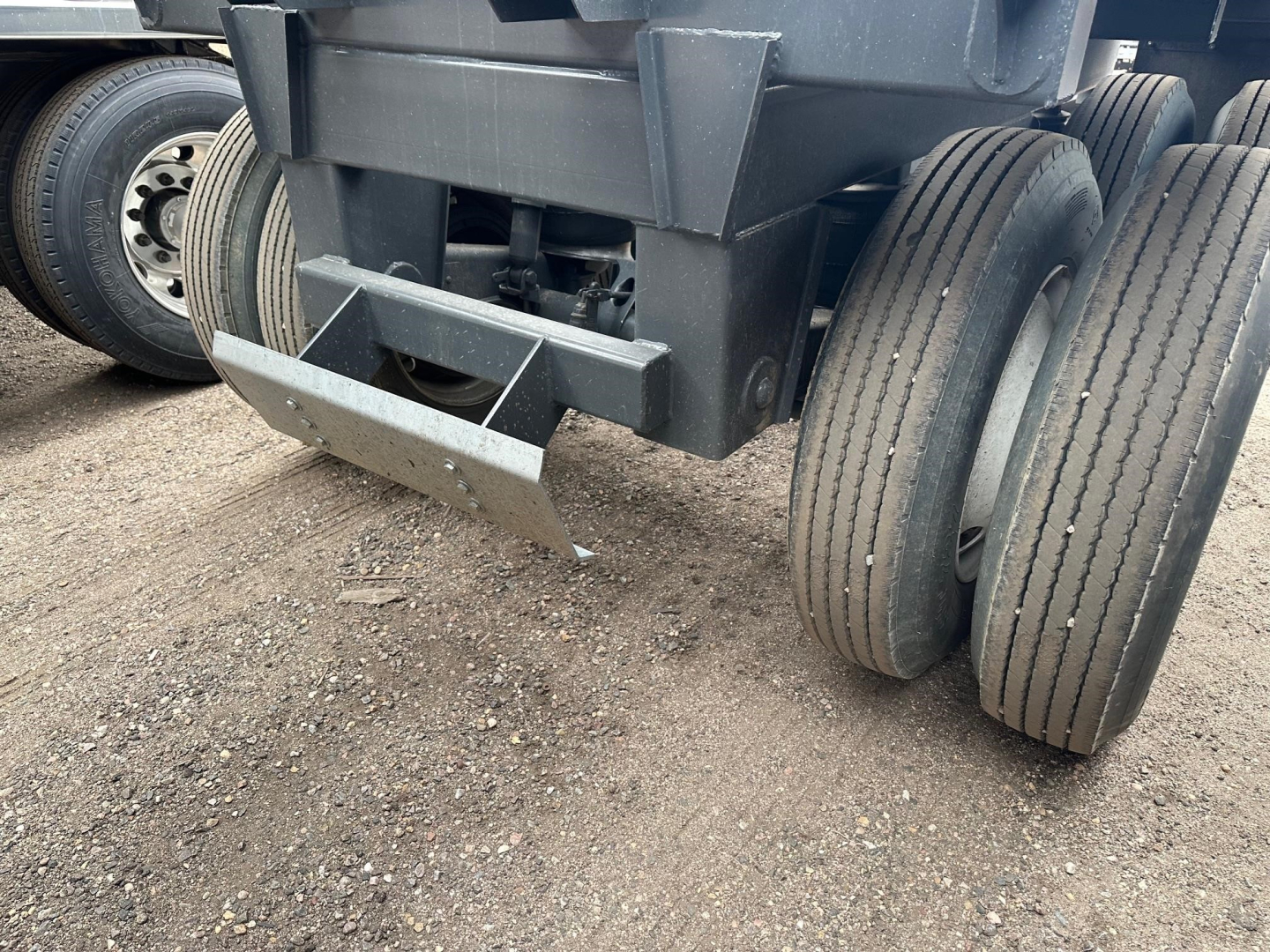 Bottom dump trailer axle and tires showing dual rear axles and towing hitch in concrete lot.