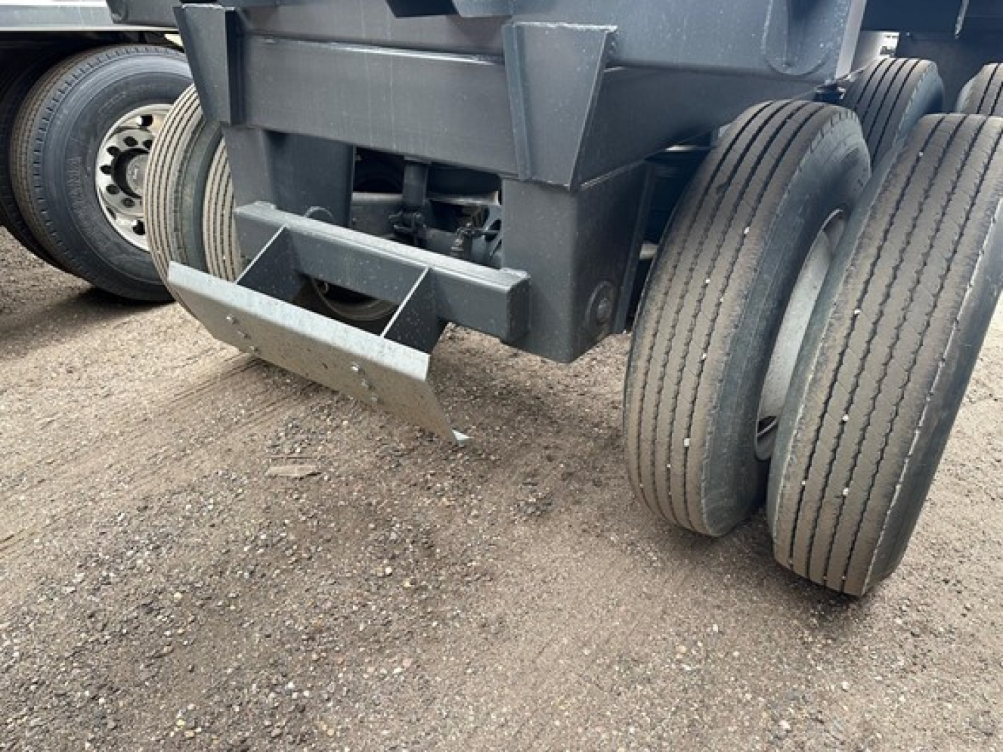 Trailer underside with dual rear axles and suspension, showing tire treads and the bottom dump mechanism; no legible text visible on components.