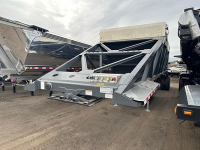 Truck trailer bottom dump with air ride system, gray metal frame, rear linkage, and control boxes. Visible text includes warning labels and small stickers on the frame.