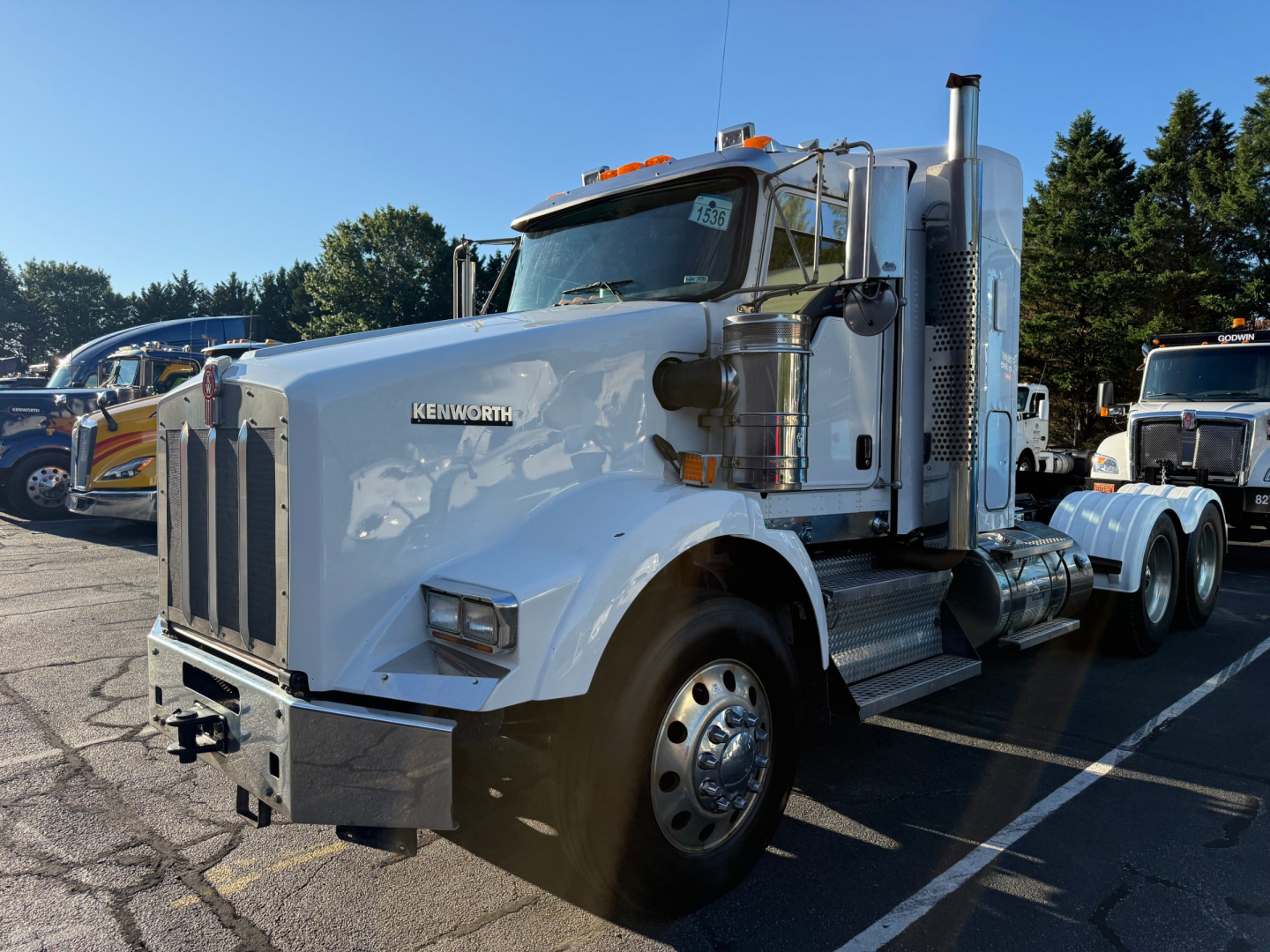 Kenworth T800 conventional sleeper truck left front view showing chrome fuel tanks and air intake, white paint, large grille, and dual rear axles.