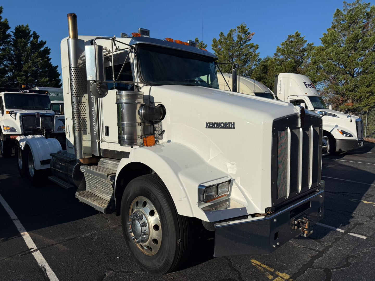 Kenworth T800 conventional sleeper truck with white cab, large chrome exhaust stacks, and black front bumper. Visible text includes 'KENWORTH' on the hood and a chrome grille.