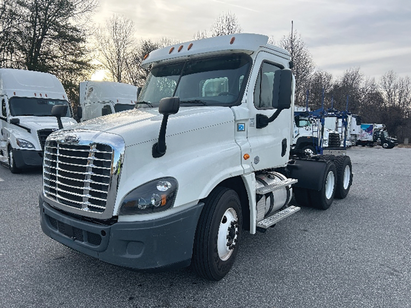 Truck cab view of a white 2018 Freightliner Cascadia125 daycab with dual rear axles, front grille, and side mirrors.