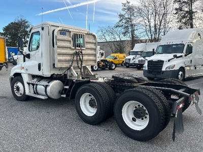 Freightliner Cascadia125 truck chassis with cab and dual rear axles visible; white cab, gray accents, and other trucks in background.