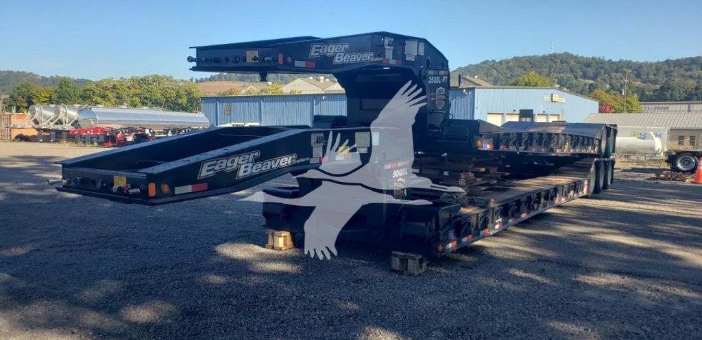 Trailer deck stacked with Eager Beaver 50Gsl-3 high-density lowboy trailer showing logos and crane arm, side view with black color and white eagle graphic.