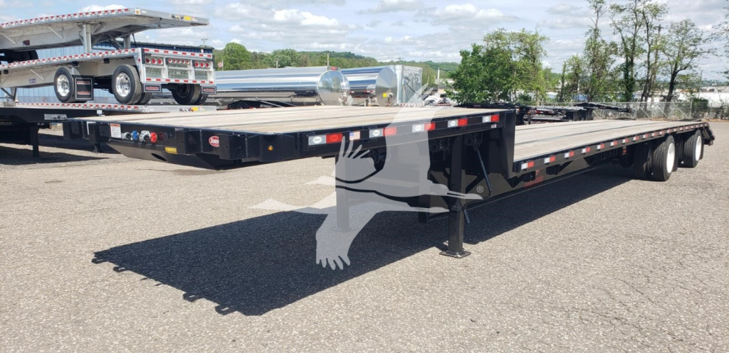 Flatbed trailer with dropdeck showing low deck height and rear ramps, light bars along top edge, and support legs extended.