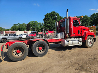 Truck chassis with red 2003 Mack CH613 cab. Dual rear axles, fuel tanks, exhaust stacks, flatbed undercarriage visible.