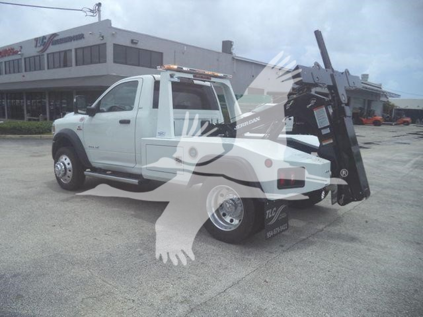 Ram tow truck with large mounted winch and forklift-style deployment arm in service bay lot.