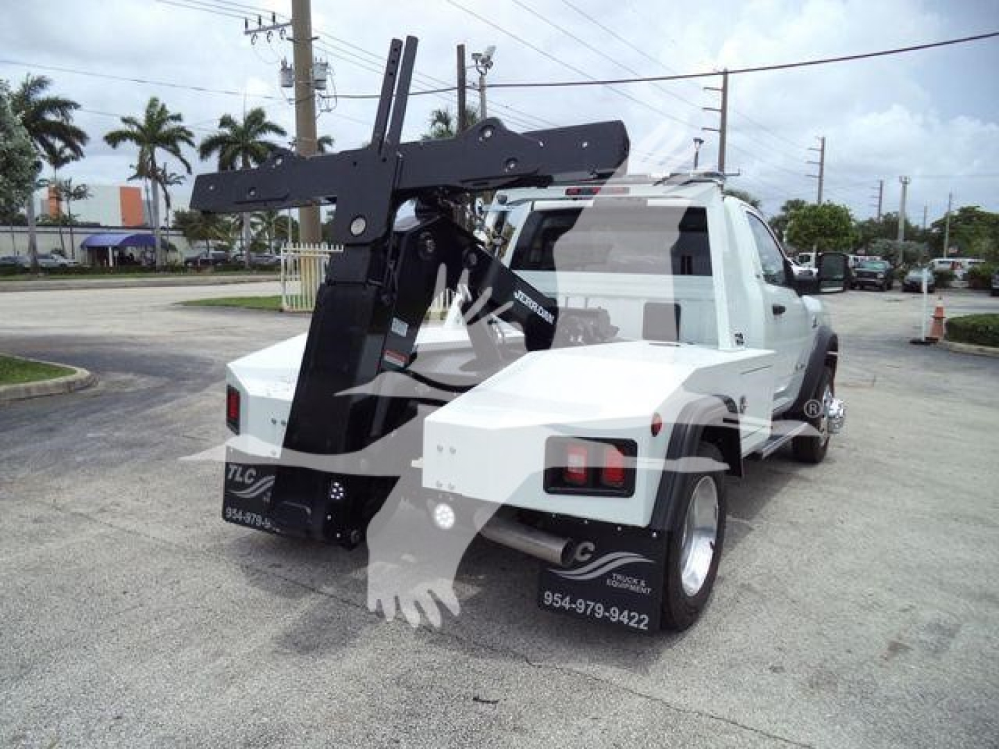 Ram 4500 truck with a mounted winch assembly on the rear, white cab and flatbed, visible stickers and contact numbers on the sides.