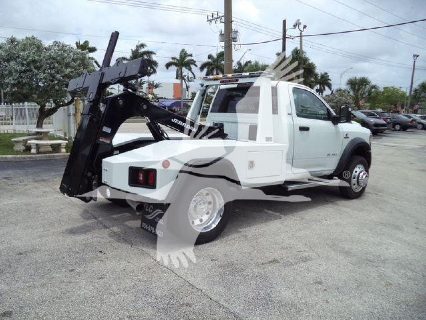 Ram 4500 tow rig with a hydraulic wench mounting and wheel-lift at rear, white cab, black hoist arm, side view showing tires and truck bed.