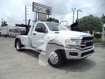 2024 Ram 4500 SLT tow truck with white cab and low-profile utility bed, front grille RAM badge, large dual rear wheels, signboards in background.