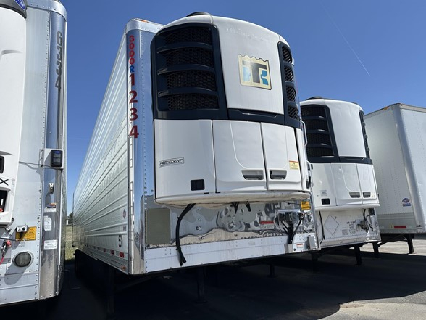 Utility 3000R trailer refrigeration unit mounted on front with white body and black grille, other trailers visible in a row.