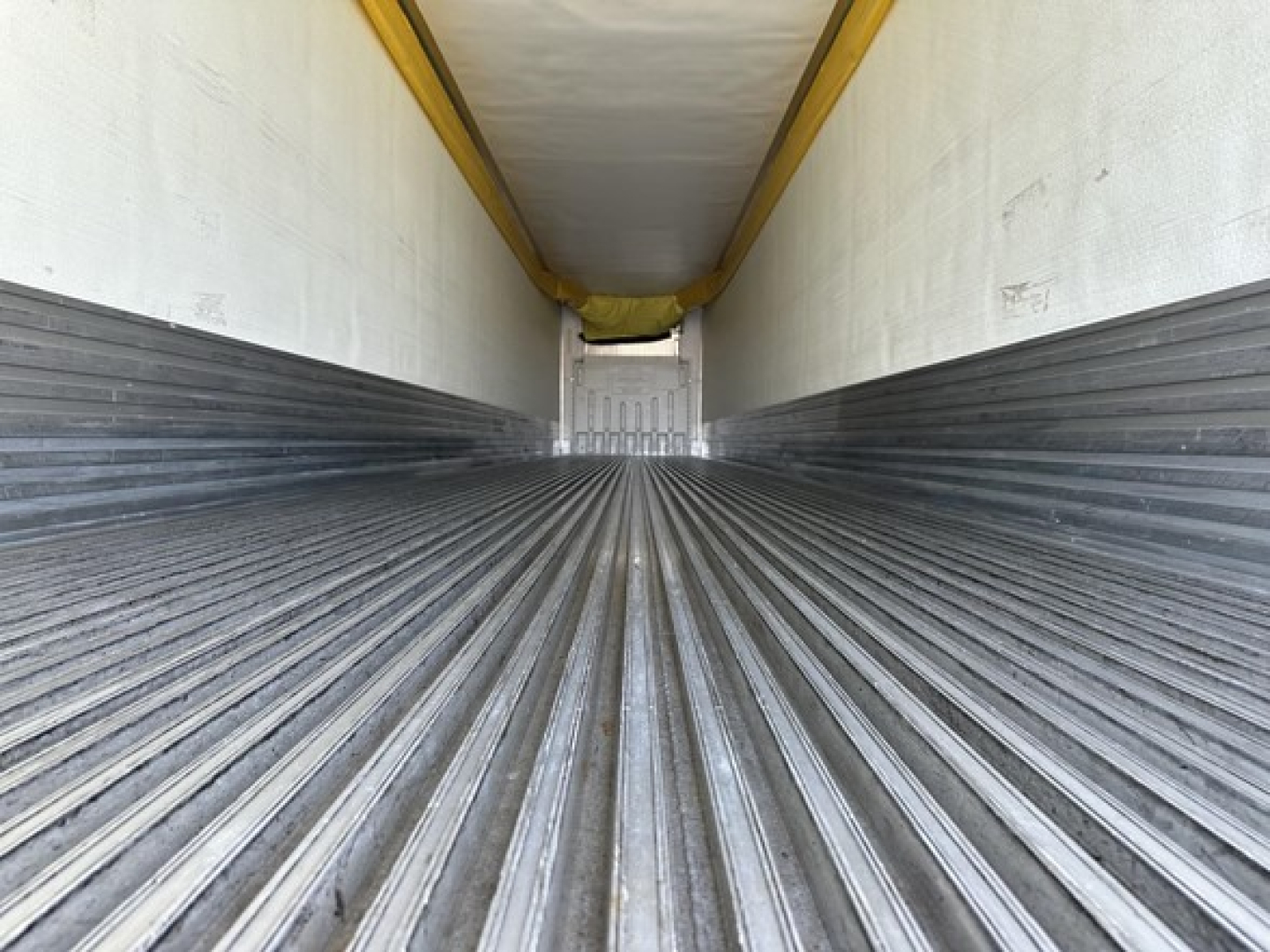Trailer interior showing corrugated metal floor and side walls with a narrow rear opening; white ceiling with yellow lip.