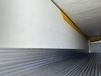 Trailer interior showing cargo area with white side panel and ribbed metal floor, overhead yellow edge seal, interior walls empty.
