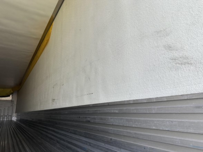 Trailer side shown with white upper wall and a ribbed metal lower edge; yellow curtain or tarp at top left. No legible model text visible.