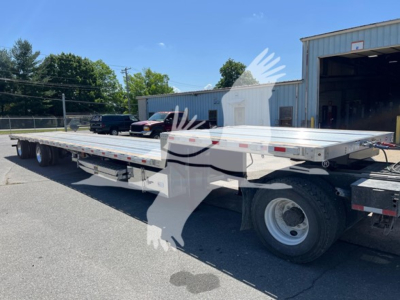 Flatbed trailer with ramp kit showing aluminum deck, black chassis, tandem rear axles, and white wheels; no visible branding text readable on image.