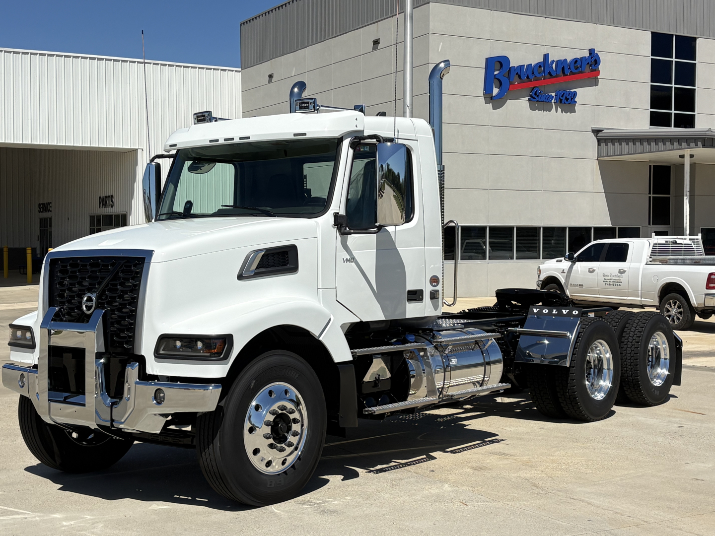 New Volvo VHD64FT300 daycab truck in white with chrome accents parked outside dealership.