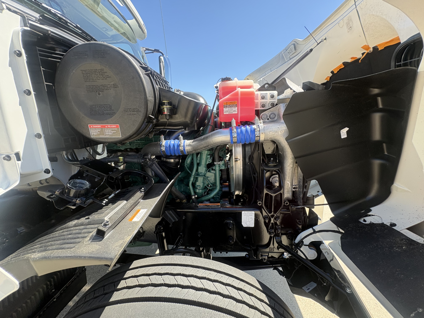 Engine bay of a Volvo VHD64FT300 cabover truck showing blue silicone hoses, air intake system, red coolant cap, and diesel engine block.