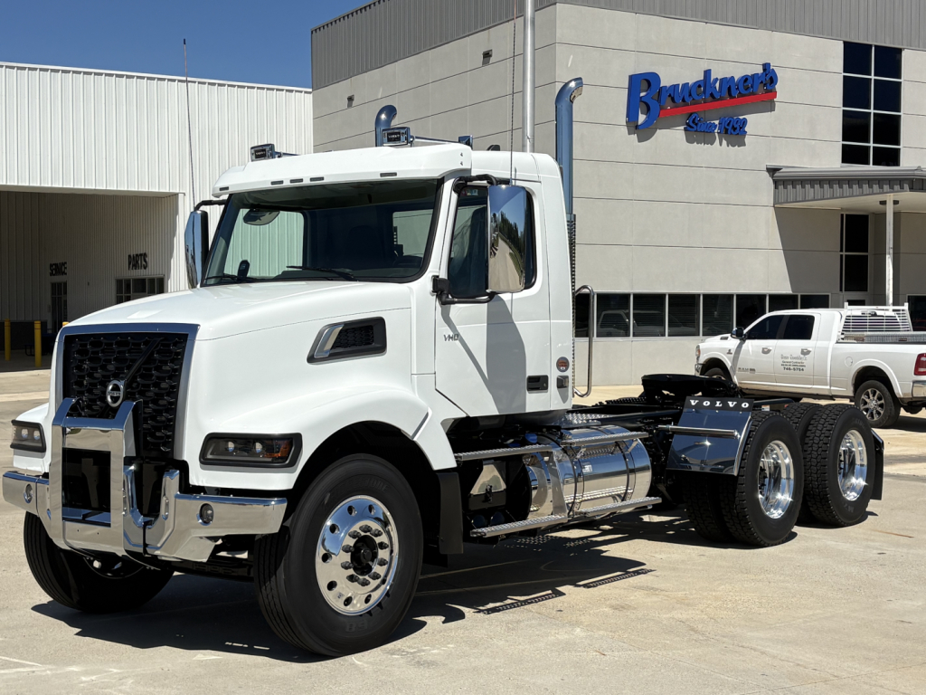New Volvo VHD64FT300 daycab truck in white with chrome accents parked outside dealership.