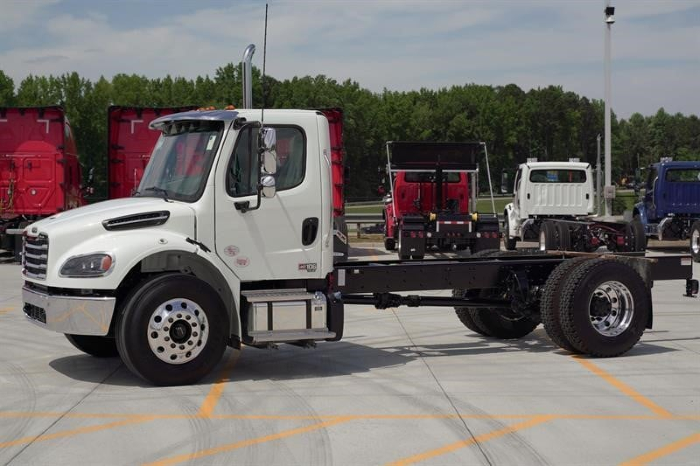 White Freightliner Business Class M2 106 Plus cab and chassis truck with empty chassis frame and front cab, on a dealership lot.