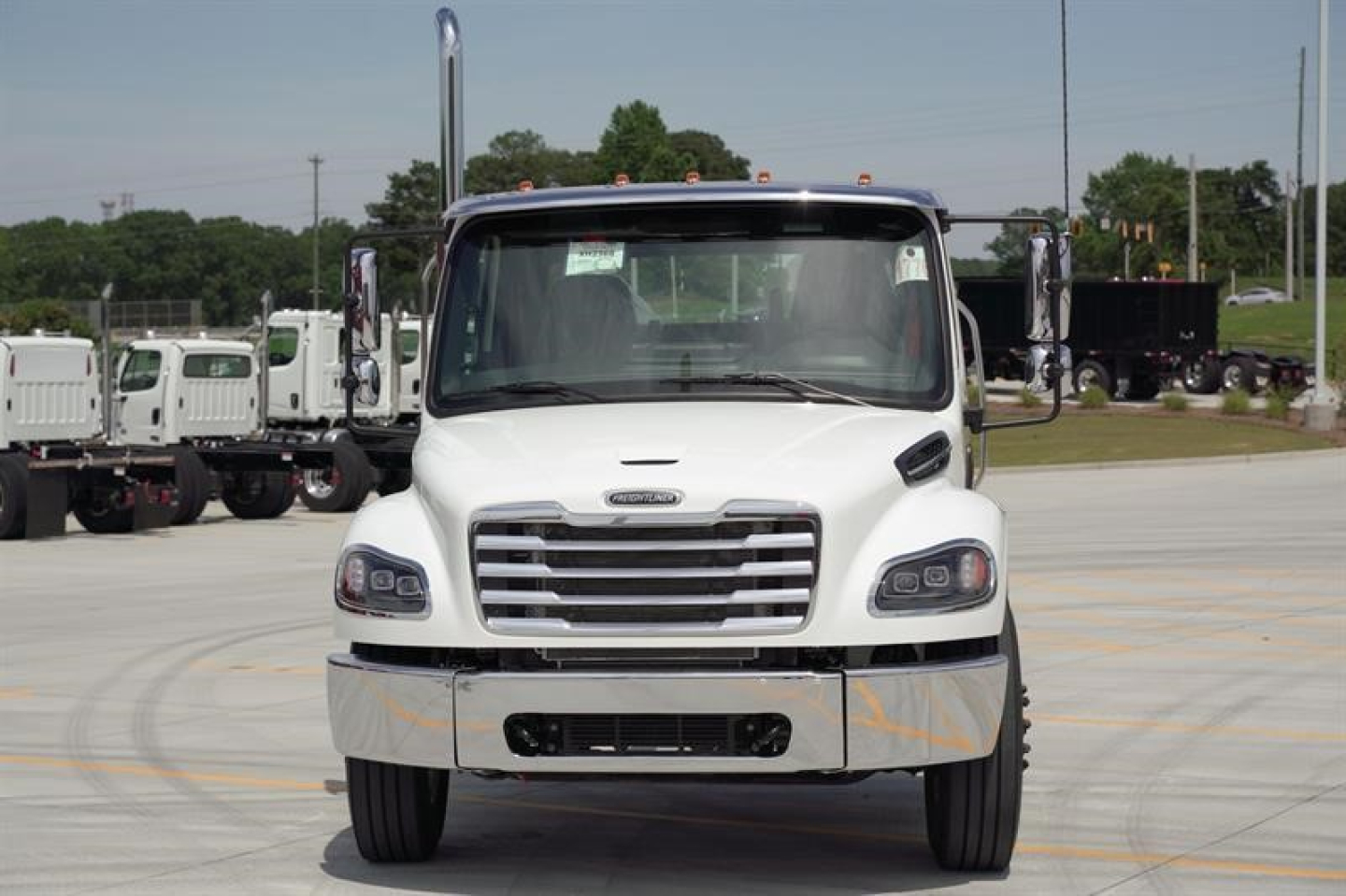Front view of a white Freightliner Business Class M2 106 Plus cab and chassis truck, with chrome grille, large side mirrors, and black front bumper, parked on a lot.