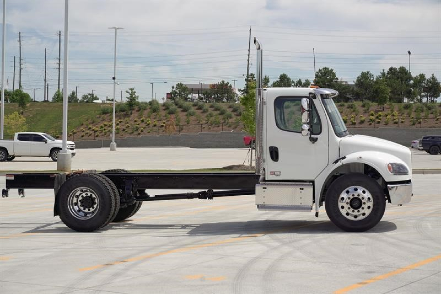Truck cab and chassis showing Freightliner Business Class M2 106 Plus style, white cab, flatbed/haul with long chassis and dual rear wheels.