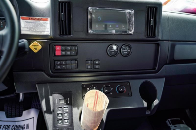 Cab interior panel of a Freightliner Business Class M2 showing dashboard controls, steering wheel, and center console with switches, gauges, and a wrapped label on the gear area.