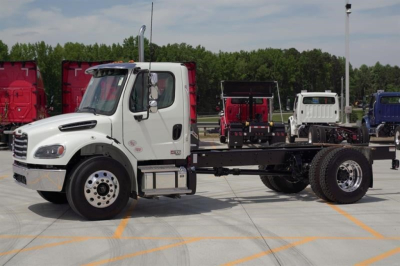 White Freightliner Business Class M2 106 Plus cab and chassis truck with empty chassis frame and front cab, on a dealership lot.