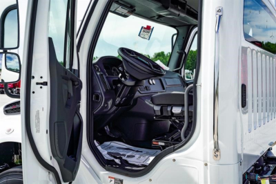 Cab and chassis truck interior visible through open driver door showing steering wheel and dashboard of a 2027 Freightliner Business Class M2 106 Plus.