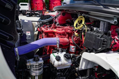 Freightliner M2 106 engine bay showing red engine, purple coolant hose, yellow cables, and various hoses and reservoirs.