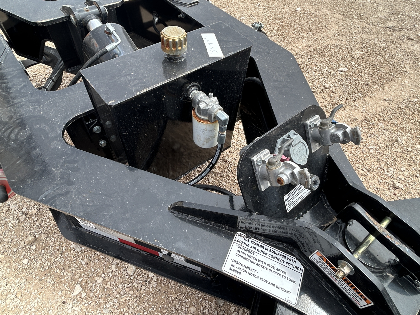 Load King trailer hitch assembly showing hydraulic and control components, caps, and warning labels on black steel frame.