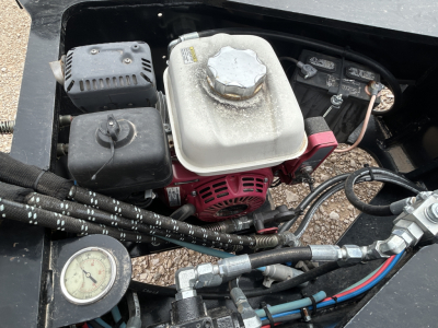Engine compartment of Load King trailer showing white coolant reservoir, red generator/air engine, black hydraulic lines, and a pressure gauge.