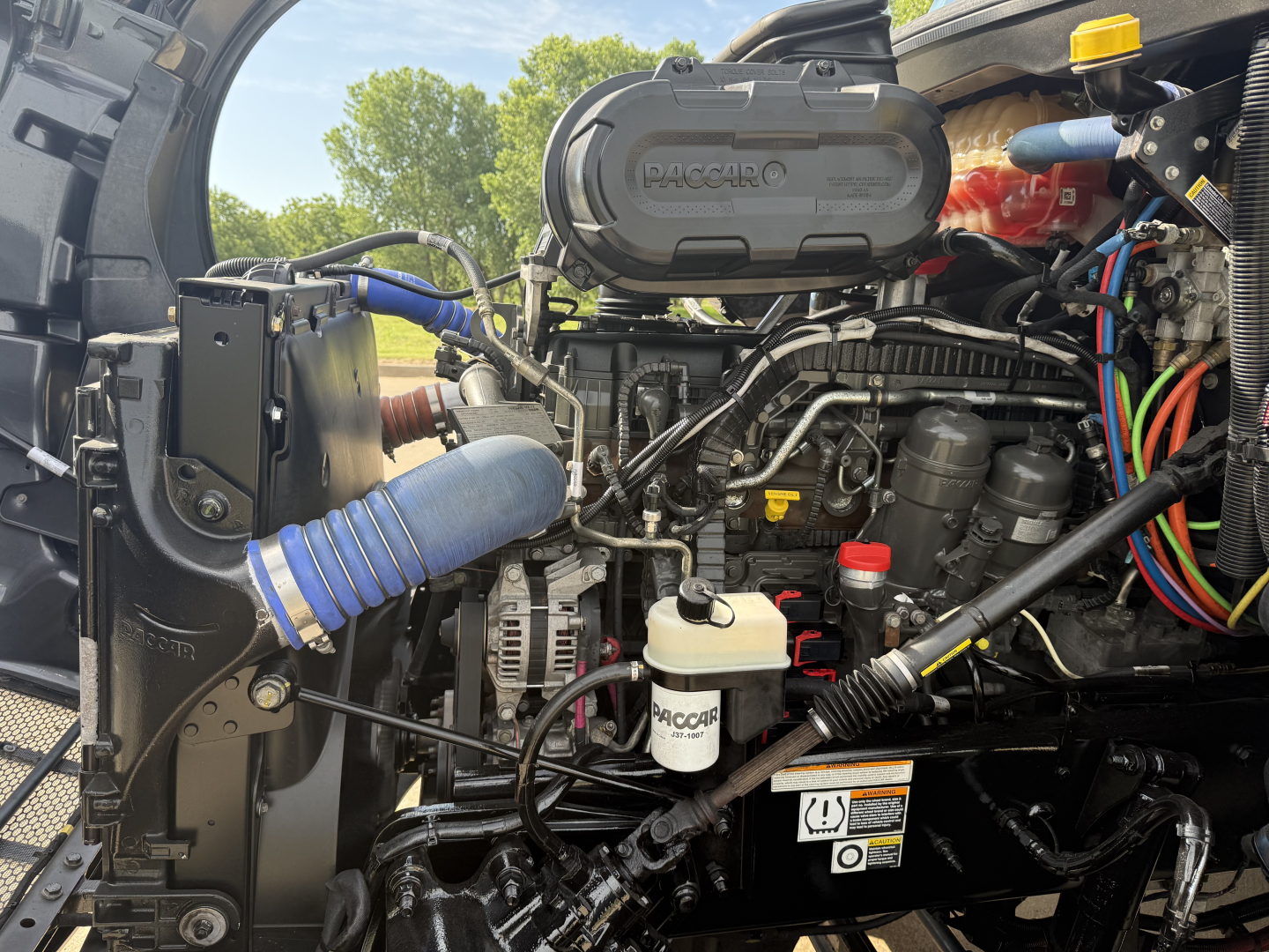 Peterbilt 579 engine bay with PACCAR-branded air intake, various hoses, hoses, and fluid reservoirs visible.