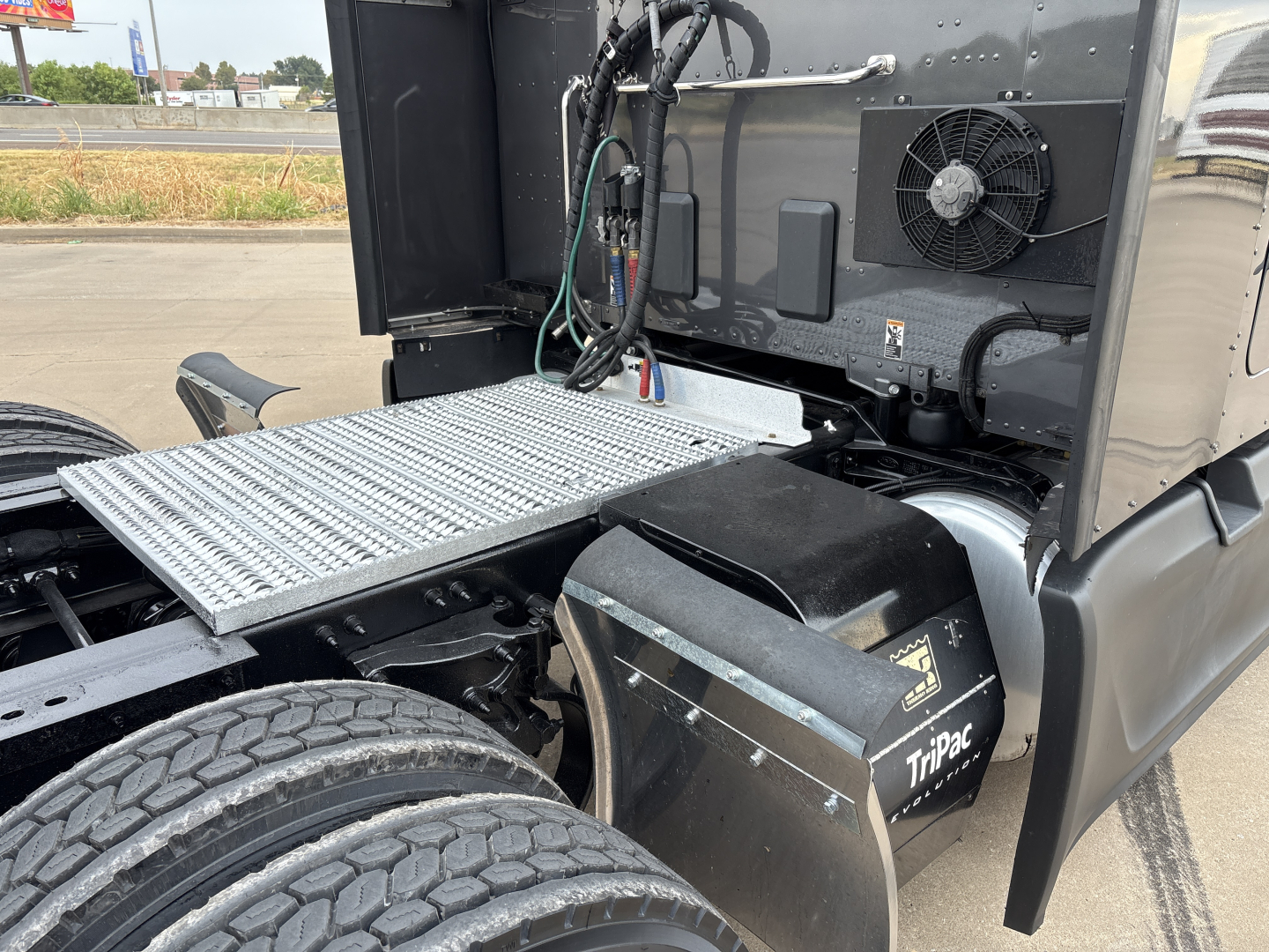 Peterbilt 579 engine bay area showing battery box and platform steps with visible cooling fan and wiring inside cab area.