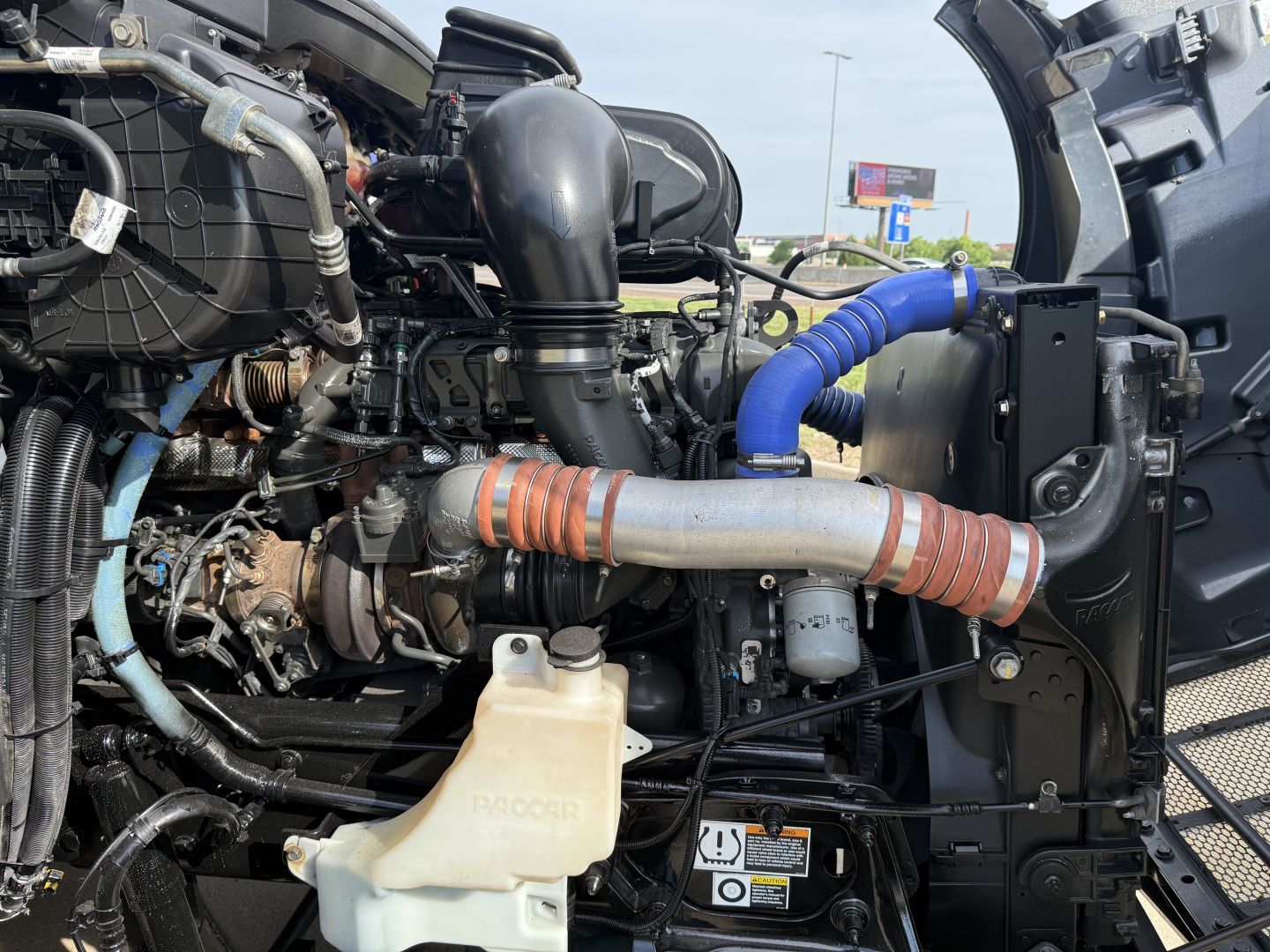 Peterbilt 579 engine bay showing intercooler piping and coolant reservoir with blue silicone hose in foreground.