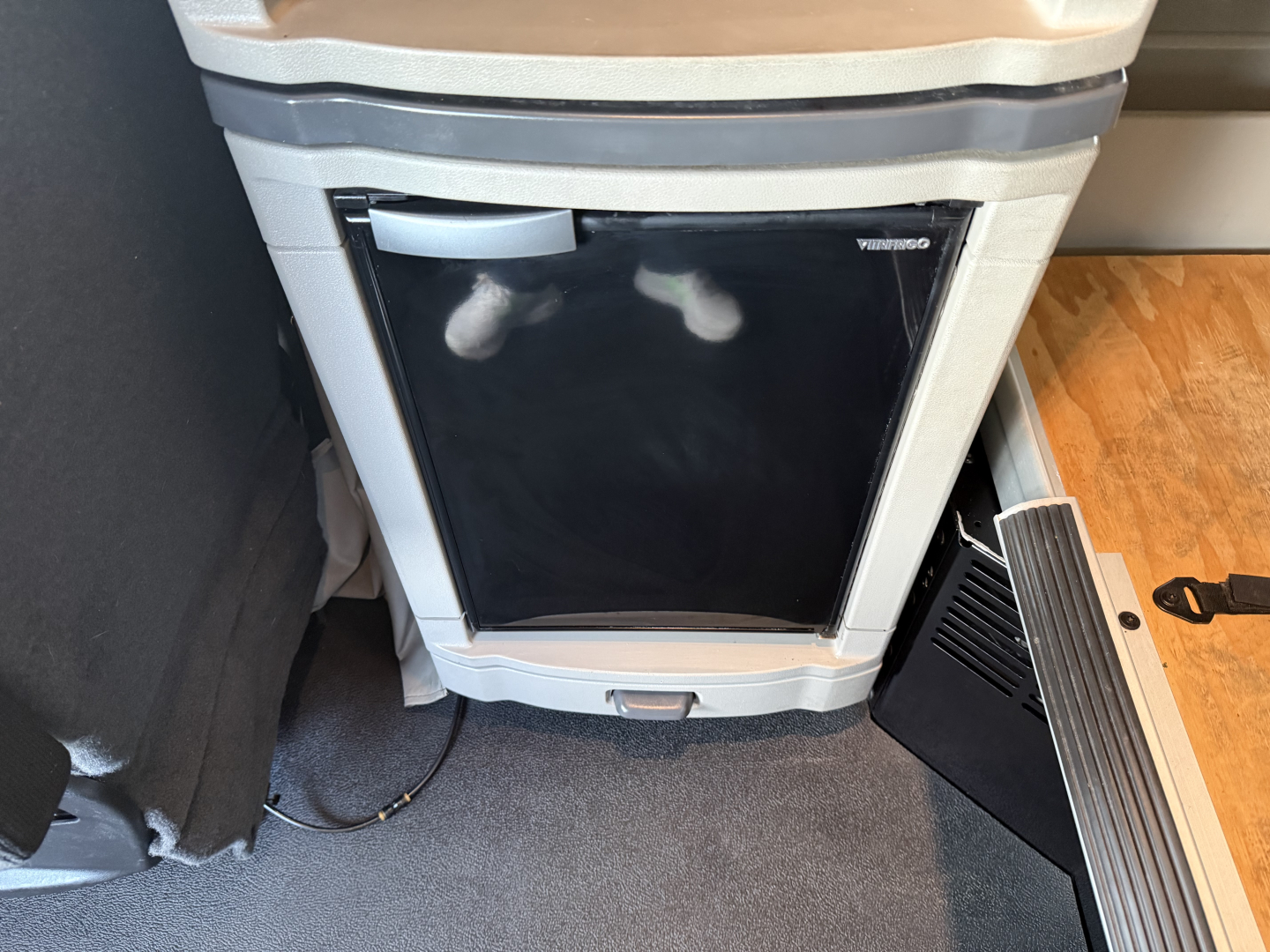 Refrigerator panel and interior in a Peterbilt 579 truck cab, showing a small fridge with black door and chrome handle, adjacent control panel area.